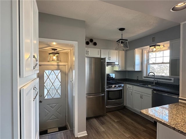 kitchen featuring pendant lighting, sink, dark stone countertops, white cabinetry, and stainless steel appliances