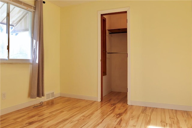 unfurnished bedroom with a spacious closet, a closet, and light hardwood / wood-style floors