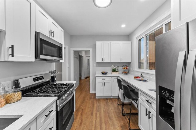 kitchen with light stone counters, white cabinetry, stainless steel appliances, and light hardwood / wood-style flooring