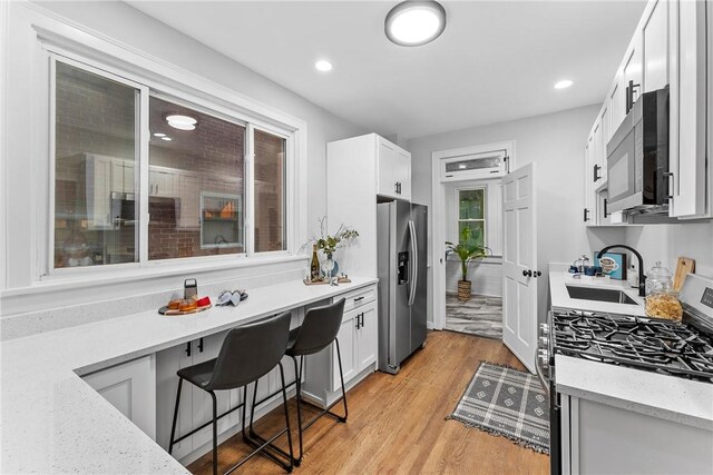 kitchen with light stone countertops, stainless steel appliances, sink, light hardwood / wood-style flooring, and white cabinets