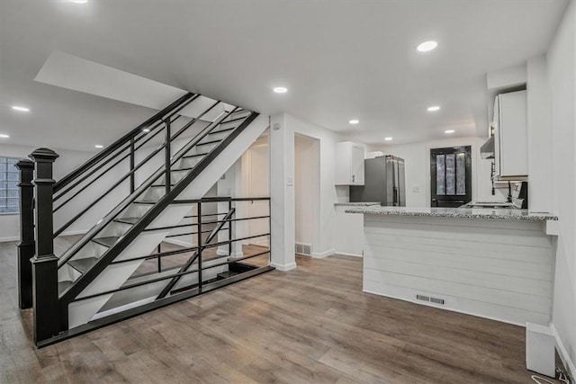 kitchen featuring stainless steel refrigerator, light stone counters, kitchen peninsula, and white cabinets