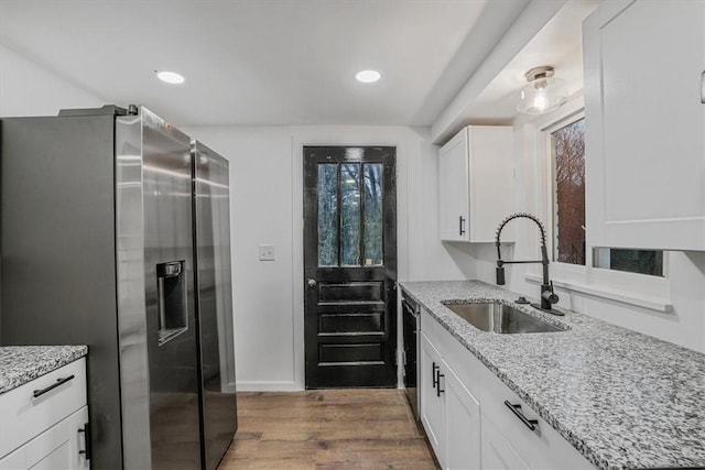 kitchen with light stone countertops, appliances with stainless steel finishes, sink, hardwood / wood-style flooring, and white cabinetry