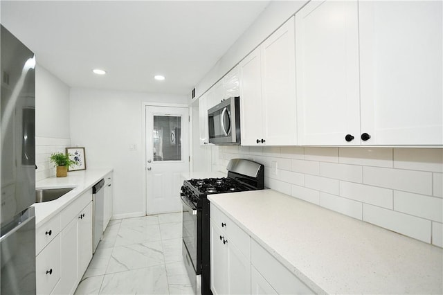 kitchen with decorative backsplash, appliances with stainless steel finishes, light stone counters, sink, and white cabinetry