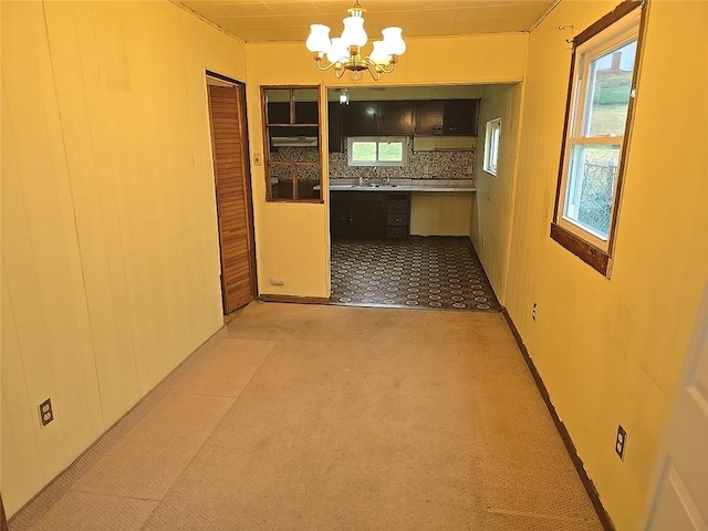 interior space featuring decorative backsplash, light carpet, sink, pendant lighting, and an inviting chandelier