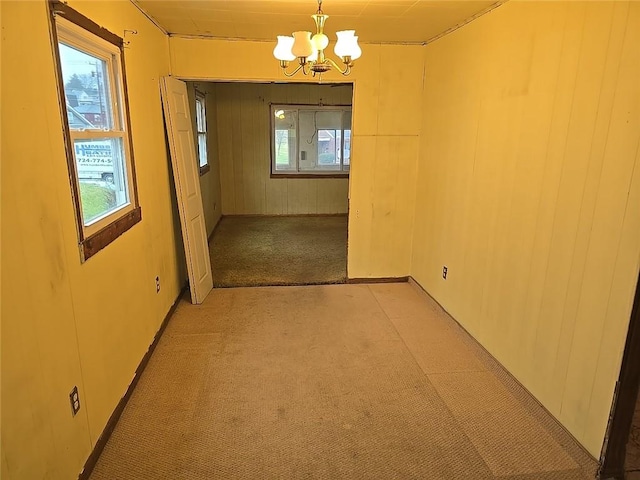 carpeted spare room with a wealth of natural light and an inviting chandelier