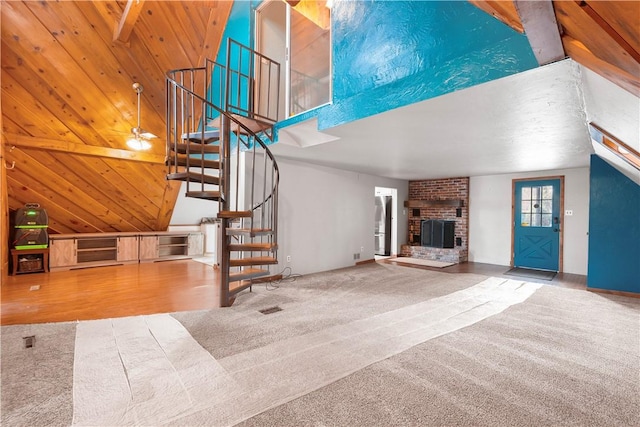 unfurnished living room featuring carpet, wooden ceiling, ceiling fan, a fireplace, and beamed ceiling