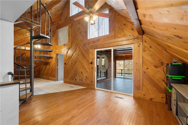 unfurnished living room with ceiling fan, high vaulted ceiling, beamed ceiling, hardwood / wood-style floors, and wood walls