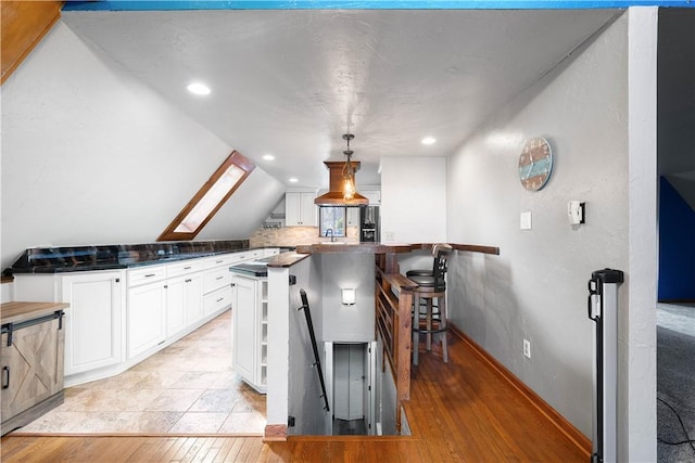 kitchen featuring white cabinets, hanging light fixtures, vaulted ceiling with skylight, light wood-type flooring, and kitchen peninsula