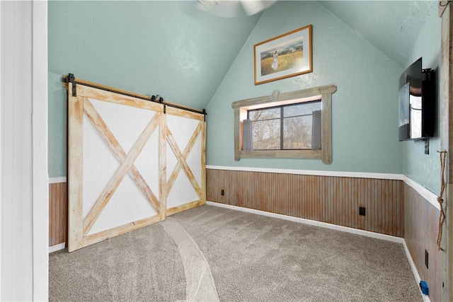 interior space featuring carpet, a barn door, lofted ceiling, and wooden walls