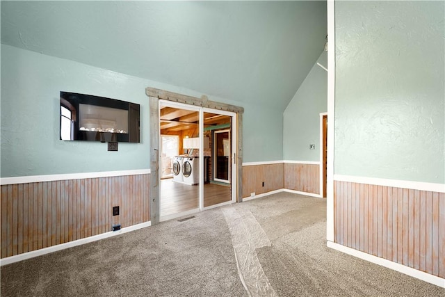 empty room with carpet flooring, washer and dryer, wooden walls, and vaulted ceiling