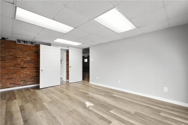 empty room with a drop ceiling, light hardwood / wood-style floors, and brick wall