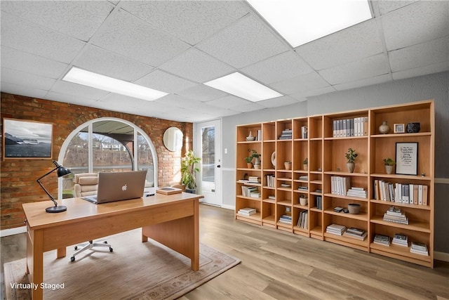 office with hardwood / wood-style floors, a drop ceiling, and brick wall