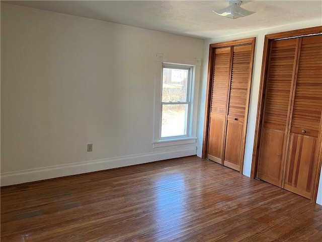 unfurnished bedroom with ceiling fan, dark wood-type flooring, and two closets