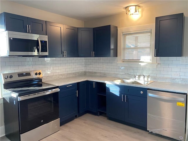 kitchen featuring appliances with stainless steel finishes, tasteful backsplash, blue cabinets, sink, and light hardwood / wood-style flooring