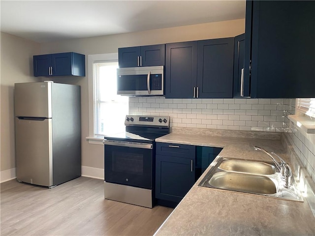 kitchen featuring appliances with stainless steel finishes, backsplash, light wood-type flooring, sink, and blue cabinetry