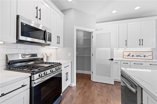 kitchen featuring light stone countertops, tasteful backsplash, appliances with stainless steel finishes, white cabinets, and light wood-type flooring