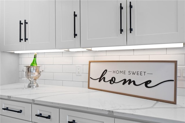 room details with white cabinets, decorative backsplash, and light stone countertops