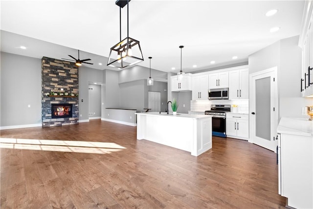 kitchen with a center island with sink, sink, hanging light fixtures, appliances with stainless steel finishes, and white cabinetry