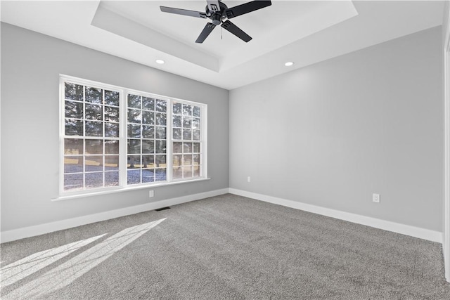 carpeted spare room with ceiling fan and a raised ceiling