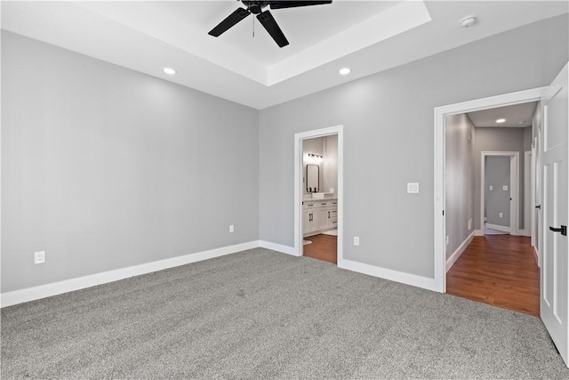 unfurnished bedroom with carpet flooring, a raised ceiling, ensuite bathroom, and ceiling fan