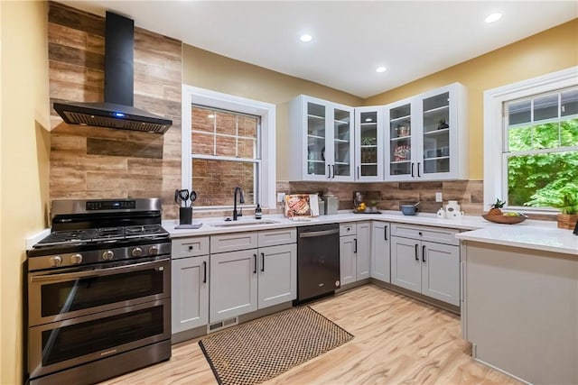 kitchen with appliances with stainless steel finishes, gray cabinetry, sink, wall chimney range hood, and light hardwood / wood-style flooring