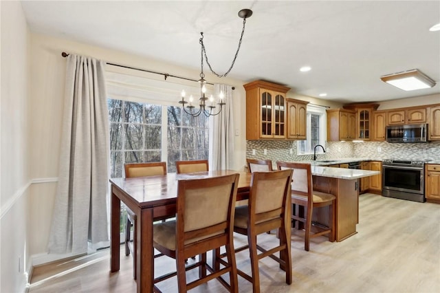 dining space with light hardwood / wood-style floors, sink, a wealth of natural light, and an inviting chandelier