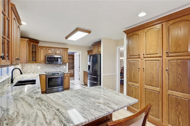 kitchen featuring light stone countertops, sink, stainless steel appliances, tasteful backsplash, and a kitchen bar