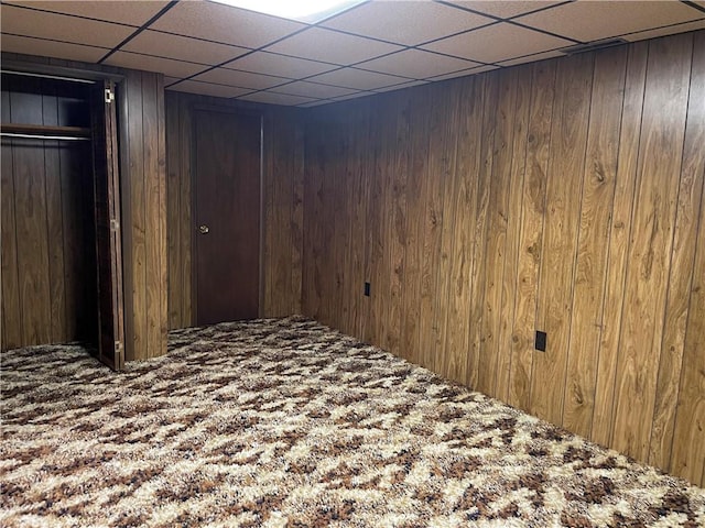 basement with a drop ceiling, carpet floors, and wooden walls