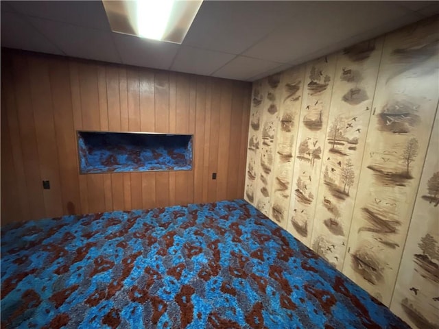 unfurnished bedroom with a paneled ceiling and wooden walls