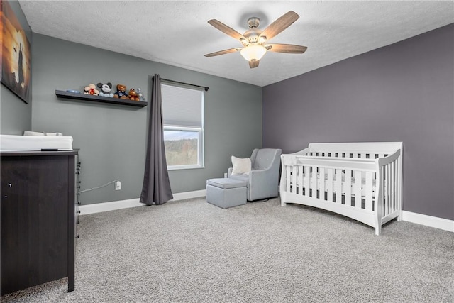 carpeted bedroom featuring a textured ceiling, ceiling fan, and a crib