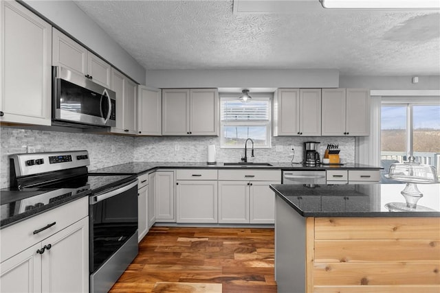 kitchen with a textured ceiling, sink, stainless steel appliances, and dark wood-type flooring