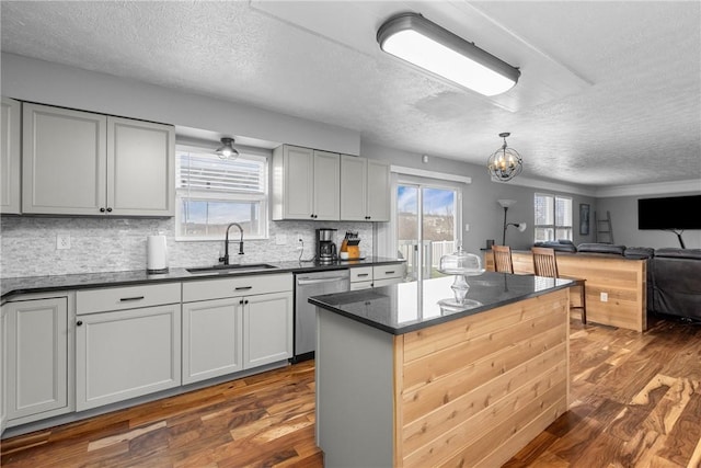 kitchen featuring backsplash, stainless steel dishwasher, dark wood-type flooring, sink, and a center island