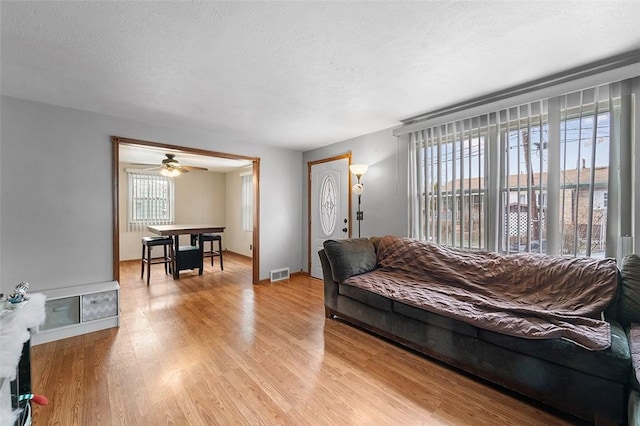 living room with ceiling fan, a textured ceiling, and light hardwood / wood-style flooring