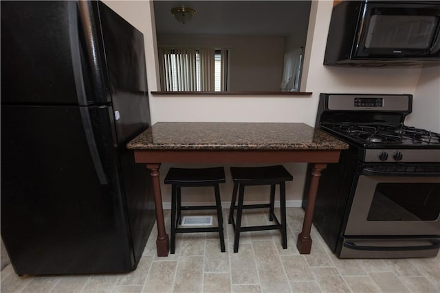 kitchen featuring black appliances, a kitchen breakfast bar, and dark stone countertops