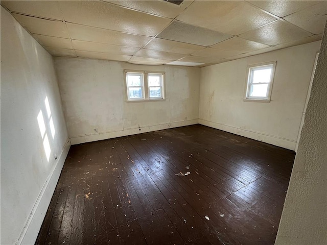 unfurnished room with plenty of natural light, a drop ceiling, and dark hardwood / wood-style floors