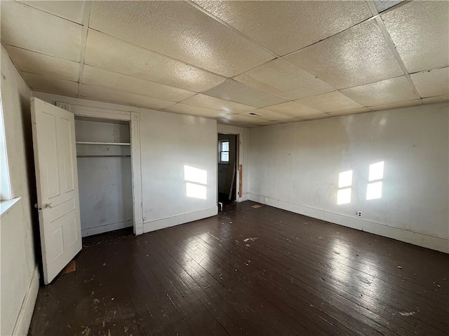 unfurnished bedroom with a closet, dark hardwood / wood-style flooring, and a drop ceiling