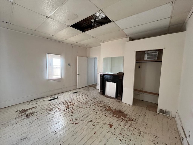 unfurnished bedroom featuring hardwood / wood-style floors, an AC wall unit, and a drop ceiling