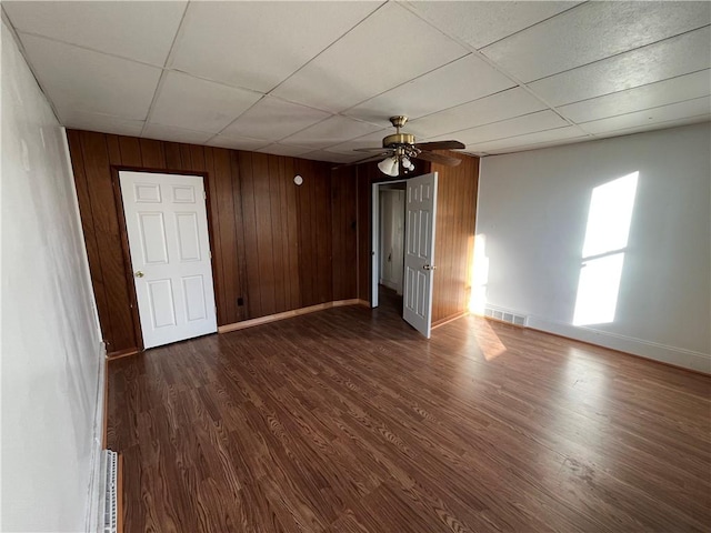 unfurnished room with a paneled ceiling, ceiling fan, wood walls, and dark hardwood / wood-style floors