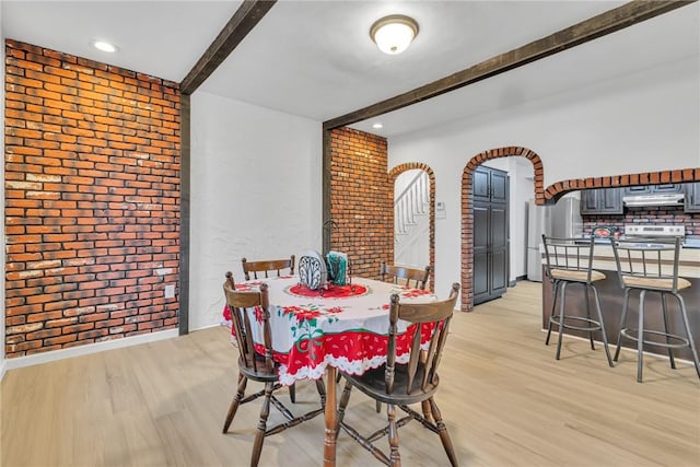 dining room featuring beam ceiling, light hardwood / wood-style floors, and brick wall