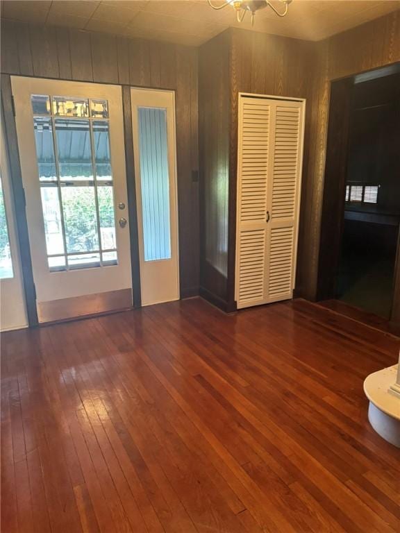 interior space featuring ceiling fan with notable chandelier, wood walls, and dark wood-type flooring