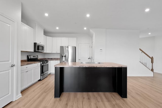 kitchen with light wood-type flooring, stainless steel appliances, a kitchen island with sink, sink, and white cabinets