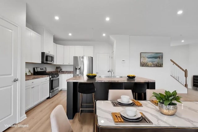 kitchen featuring appliances with stainless steel finishes, a center island with sink, light hardwood / wood-style flooring, white cabinetry, and a breakfast bar area