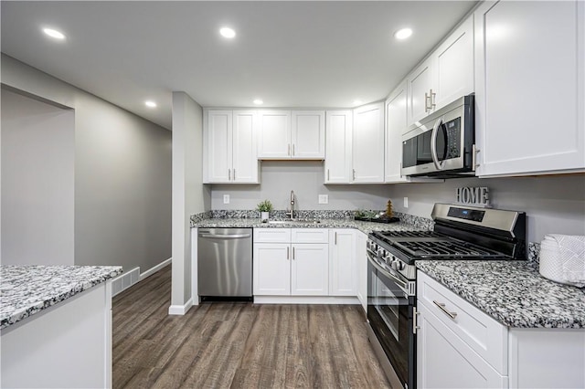 kitchen with dark hardwood / wood-style flooring, light stone counters, stainless steel appliances, sink, and white cabinets