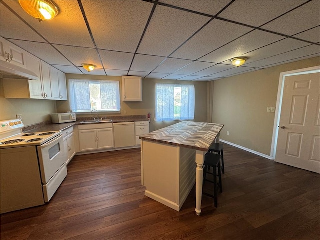 kitchen featuring a drop ceiling, white appliances, sink, white cabinets, and a breakfast bar area