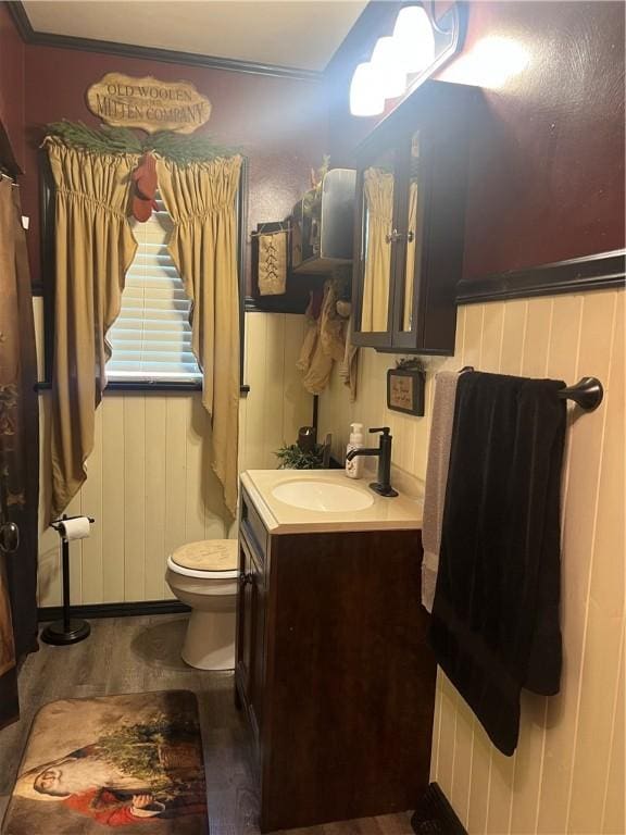 bathroom featuring vanity, wood walls, toilet, ornamental molding, and wood-type flooring