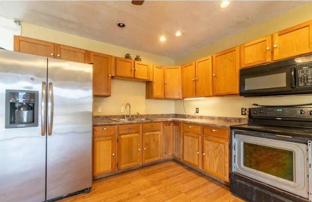 kitchen with black appliances, sink, and light hardwood / wood-style flooring