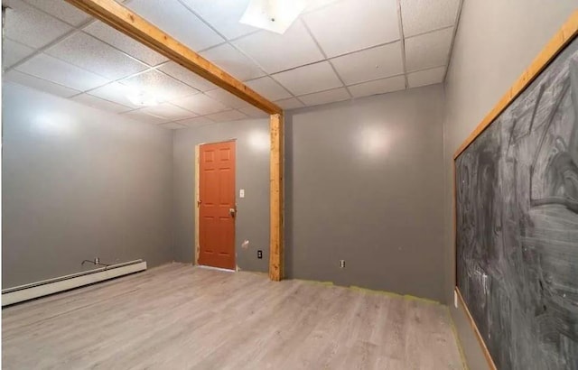 basement featuring wood-type flooring, a drop ceiling, and a baseboard heating unit