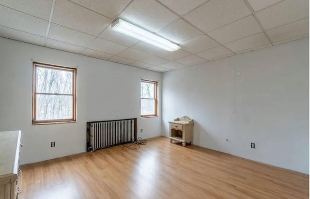 spare room featuring a paneled ceiling, radiator heating unit, and light hardwood / wood-style flooring