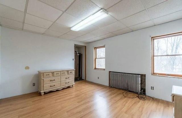 empty room with a paneled ceiling, radiator heating unit, light hardwood / wood-style floors, and plenty of natural light