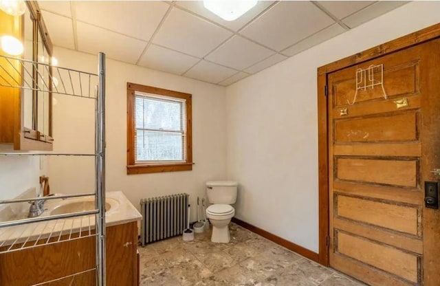 bathroom featuring radiator heating unit, vanity, toilet, and a drop ceiling